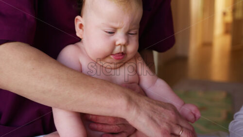 Caregiver holding a baby upright during a developmental exercise while another adult engages with a toy nearby
