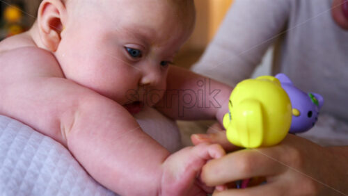 Woman trying to distract a crying baby lying on a blanket during massage with a toy