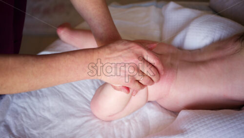 Baby lying on their tummy while an adult massages them and performs mobility exercises