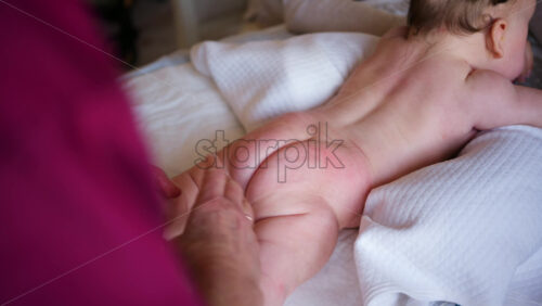 Baby lying on their tummy while an adult massages them and performs mobility exercises