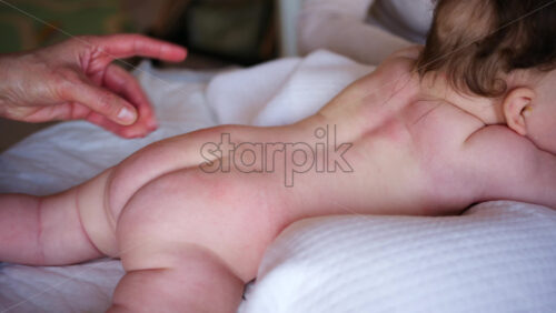 Baby lying on their tummy while an adult massages them and performs mobility exercises