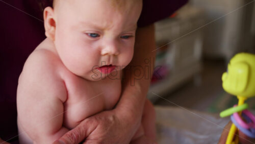 Woman trying to distract a crying baby lying on a blanket during massage with a toy