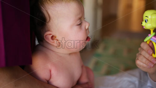 Woman trying to distract a crying baby lying on a blanket during massage with a toy