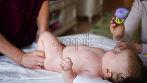 Woman trying to distract a crying baby lying on a blanket during massage with a toy
