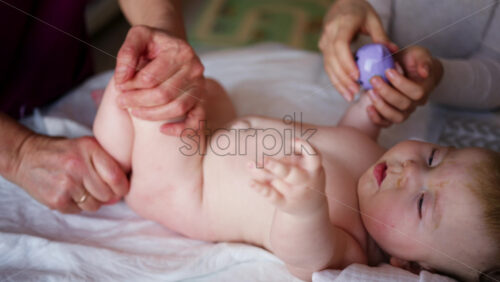 Woman trying to distract a crying baby lying on a blanket during massage with a toy
