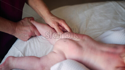 Baby lying on their tummy while an adult massages them and performs mobility exercises