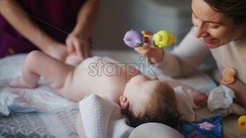 Woman trying to distract a crying baby lying on a blanket during massage with a toy