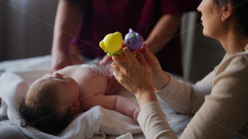 Woman trying to distract a crying baby lying on a blanket during massage with a toy