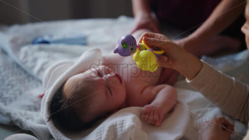 Woman trying to distract a crying baby lying on a blanket during massage with a toy
