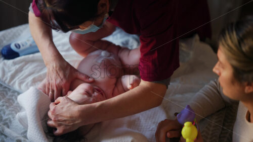 Woman trying to distract a crying baby lying on a blanket during massage with a toy