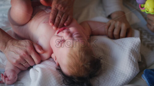 Baby lying on their back while an adult massages them and the mother gently holds the baby's hand