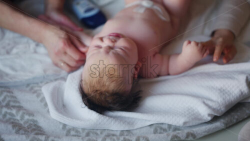 Baby lying on their back while an adult massages them and the mother gently holds the baby's hand