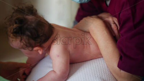 Baby placed on a stability ball while adults support the infant's body