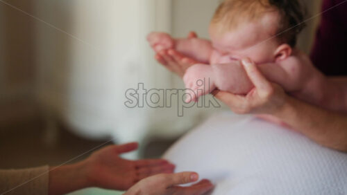 Baby placed on a stability ball while adults support the infant's body