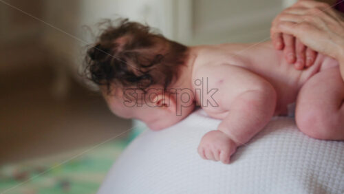 Baby lying on tummy on a ball while caregiver gently holds the lower back