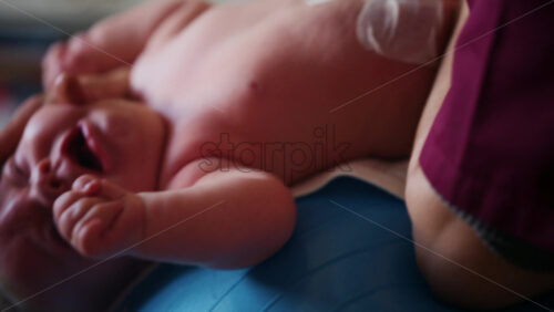 Baby placed on a stability ball while adults support the infant's body
