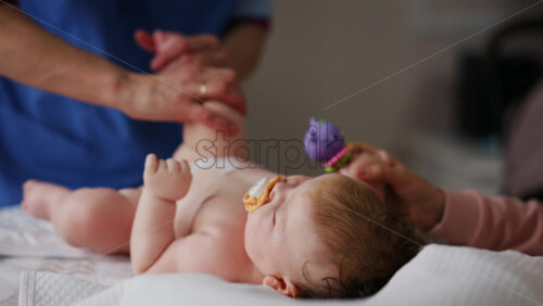 Baby lying on back with pacifier while adults assist with gentle arm and leg movements