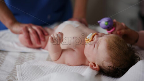 Baby lying on back with pacifier while adults assist with gentle arm and leg movements