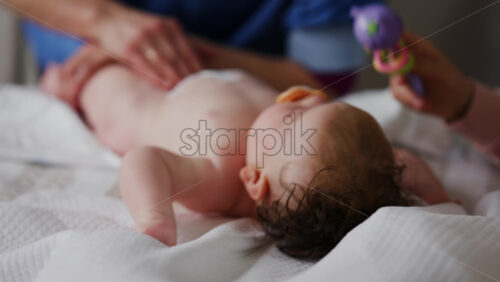 Baby lying on back with pacifier while adults assist with gentle arm and leg movements