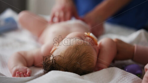 Baby lying on their back while an adult massages them and the mother gently holds the baby's hand