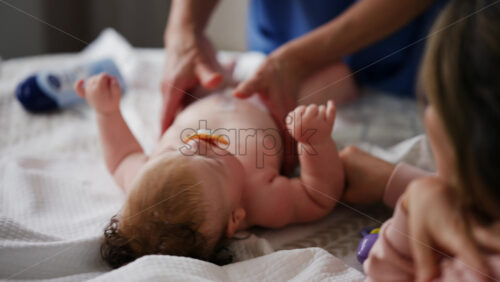 Baby lying on their back while an adult massages them and the mother gently holds the baby's hand