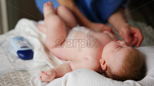 Woman trying to distract a crying baby lying on a blanket during massage with a toy
