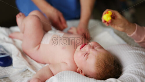 Woman trying to distract a crying baby lying on a blanket during massage with a toy