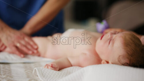 Woman trying to distract a crying baby lying on a blanket during massage with a toy