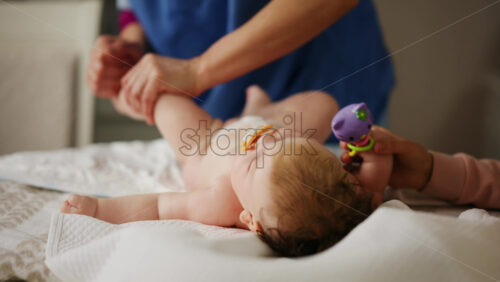 Woman trying to distract a crying baby lying on a blanket during massage with a toy