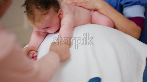 Baby placed on tummy on a stability ball while adults support the infant's torso and shoulders
