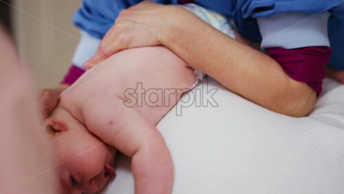 Baby placed on tummy on a stability ball while adults support the infant's torso and shoulders