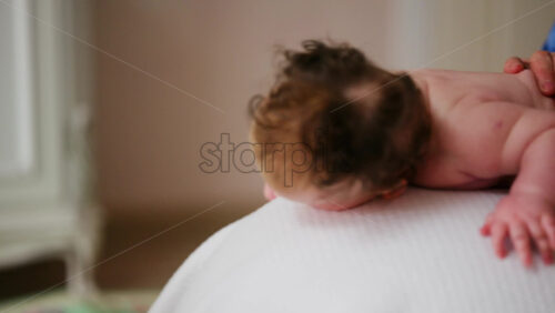 Baby placed on tummy on a stability ball while adults support the infant's torso and shoulders