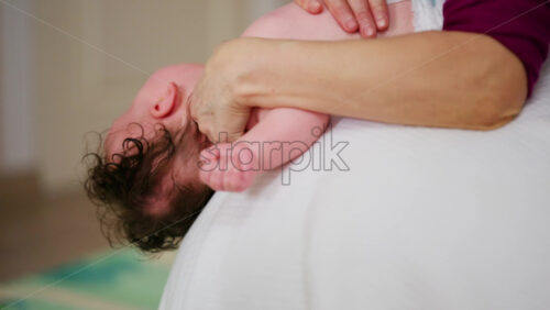 Baby placed on the back on a stability ball while adults support the infant's torso and shoulders
