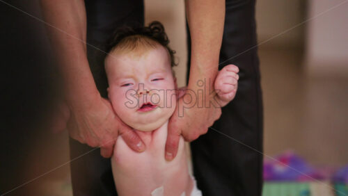 Close up of a caregiver holding a baby under the arms, helping them stand upright and walk