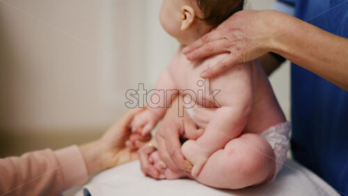 Baby placed on a stability ball while adults support the infant's body