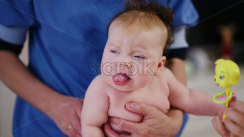 Woman trying to distract a crying baby lying on a blanket during massage with a toy