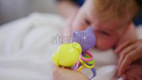 Woman trying to distract a crying baby lying on a blanket during massage with a toy