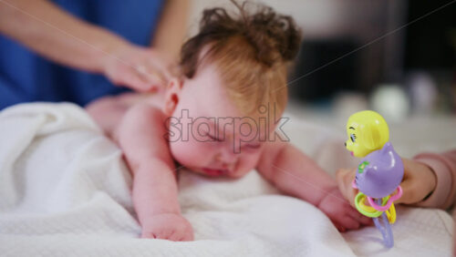 Woman trying to distract a crying baby lying on a blanket during massage with a toy