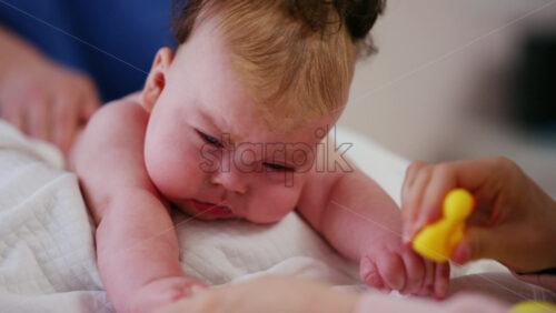 Woman trying to distract a crying baby lying on a blanket during massage with a toy