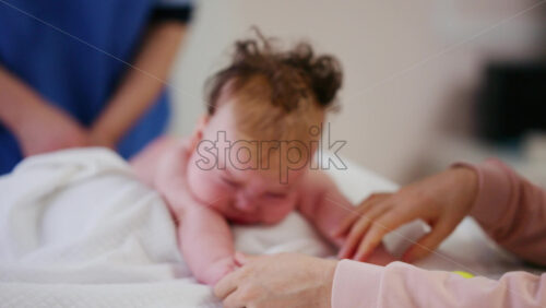 Woman trying to distract a crying baby lying on a blanket during massage with a toy