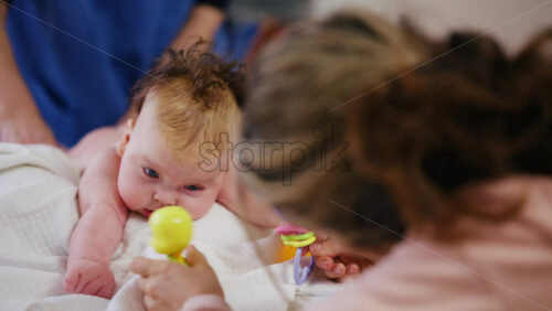 Woman trying to distract a crying baby lying on a blanket during massage with a toy