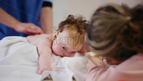 Woman trying to distract a crying baby lying on a blanket during massage with a toy
