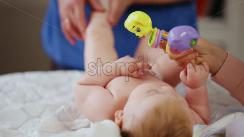 Woman trying to distract a crying baby lying on a blanket during massage with a toy
