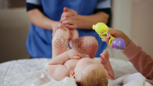 Woman trying to distract a crying baby lying on a blanket during massage with a toy