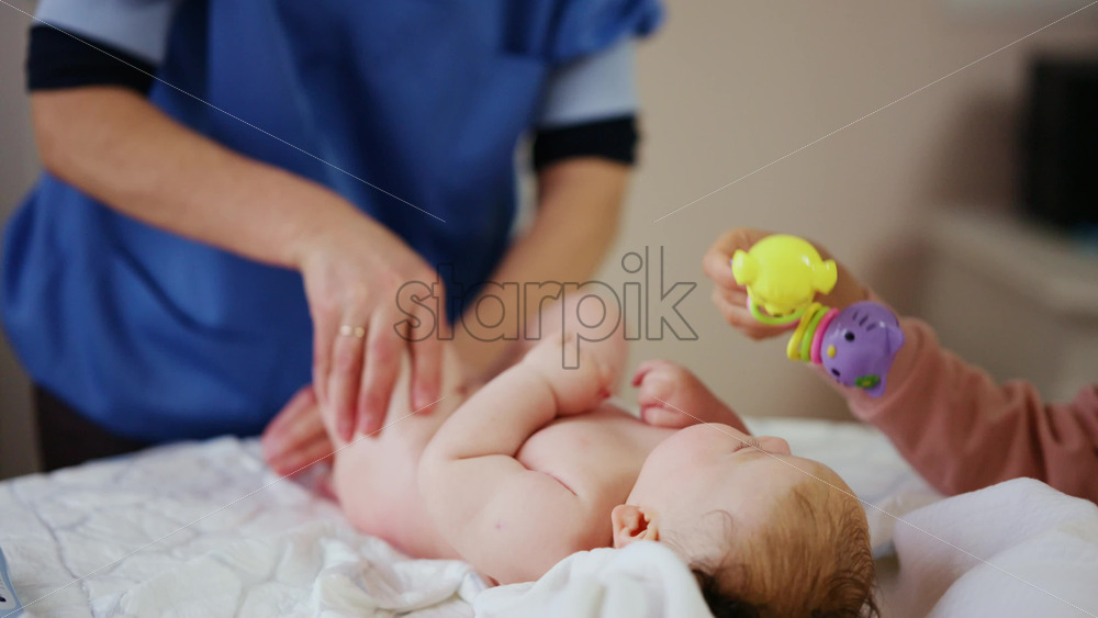 Woman trying to distract a crying baby lying on a blanket during massage with a toy