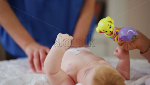 Woman trying to distract a crying baby lying on a blanket during massage with a toy