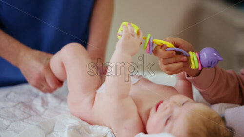 Woman trying to distract a crying baby lying on a blanket during massage with a toy