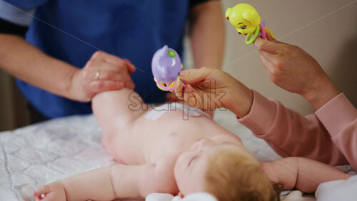 Woman trying to distract a crying baby lying on a blanket during massage with a toy