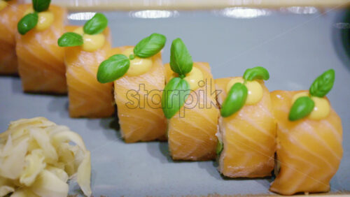 A plated dish of salmon sushi, neatly arranged with green garnish on top with soy sauce in a small bowl, plus wasabi and pickled ginger on the side