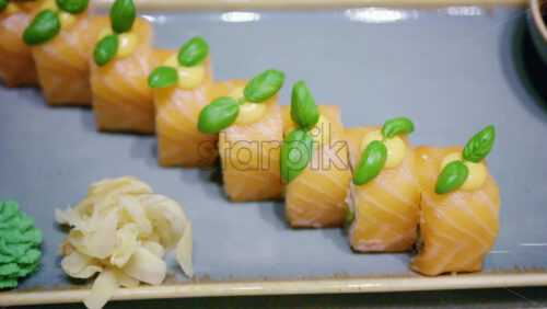A plated dish of salmon sushi, neatly arranged with green garnish on top with soy sauce in a small bowl, plus wasabi and pickled ginger on the side